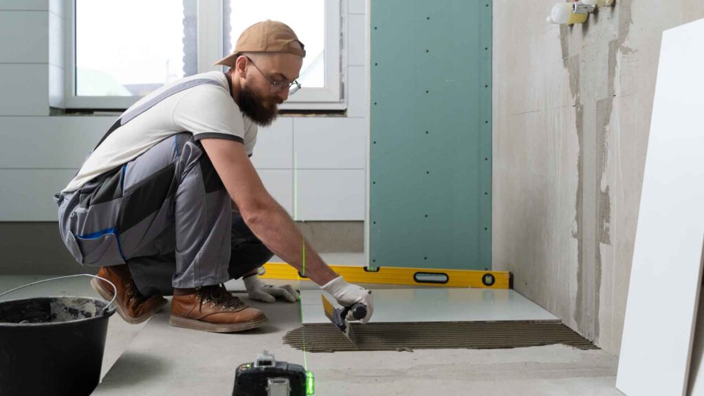 A worker carefully laying floor tiles with precision in a home interior.